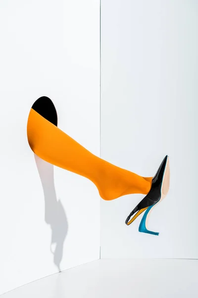 Cropped image of girl showing leg in fashionable orange tights and black high heel in hole on white — Stock Photo