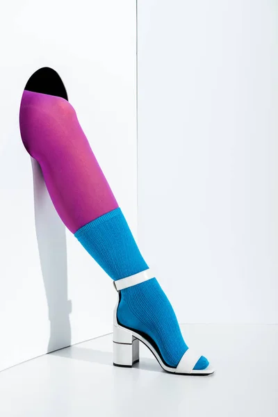 Image recadrée de fille montrant jambe en collants violets, chaussette bleue et talon haut blanc dans le trou sur blanc — Photo de stock