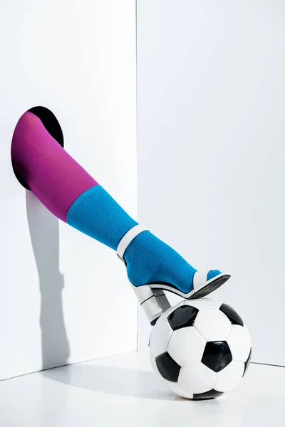 Cropped image of girl putting leg in stylish violet tights, blue sock and white high heel on football ball through hole on white — Stock Photo