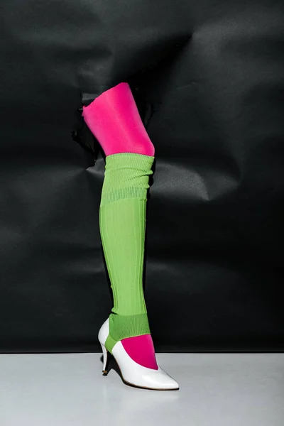 Cropped image of girl showing leg in pink tights, green gaiter and white high heel through black paper — Stock Photo