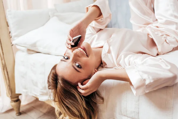 Vue rapprochée de la jeune femme souriante en pyjama parlant sur smartphone au lit à la maison — Photo de stock