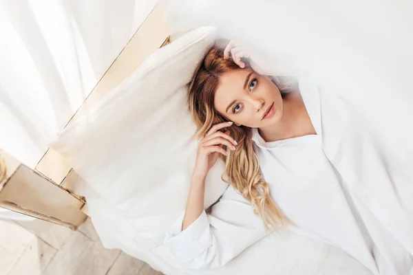 Selective focus of beautiful woman in white shirt posing in bed at home — Stock Photo