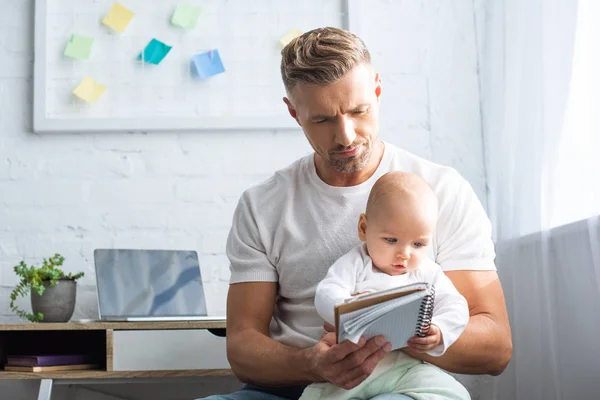 Padre sentado con la hija del bebé y sosteniendo el cuaderno en casa — Stock Photo