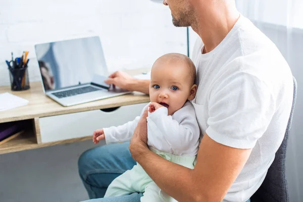 Father sitting at computer desk with credit card for online shopping and holding adorable baby daughter at home — Stock Photo