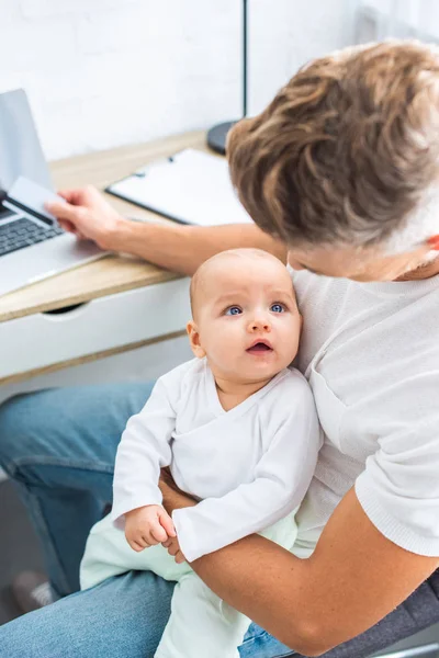 Padre sentado en el escritorio de la computadora con tarjeta de crédito y mirando a la hija bebé - foto de stock