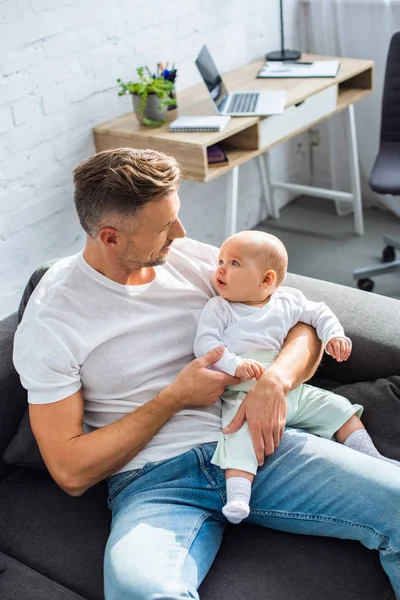 Pai sentado no sofá e segurando adorável bebê filha na sala de estar — Fotografia de Stock