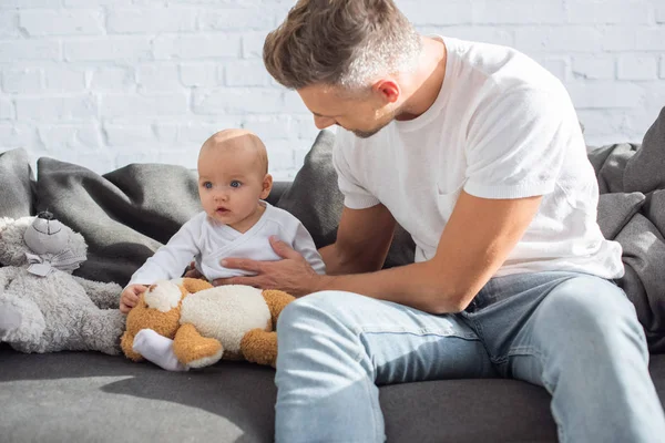 Vater und entzückende kleine Tochter sitzen mit Teddybären zu Hause auf der Couch — Stockfoto