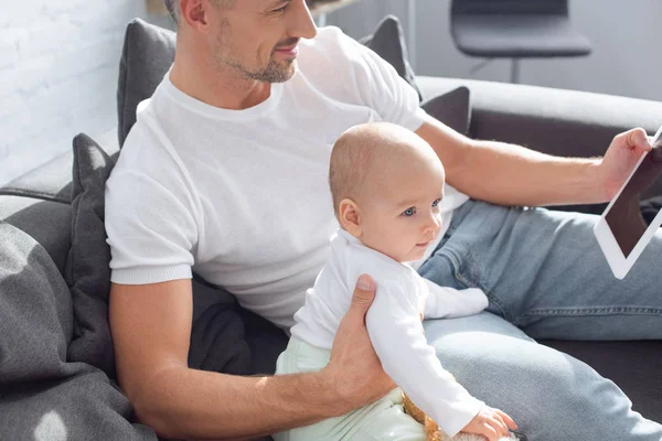 Vater sitzt mit entzückender Tochter auf Couch und nutzt zu Hause digitales Tablet — Stockfoto