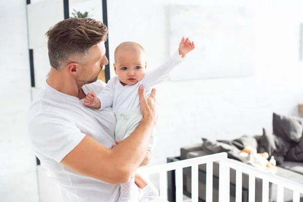 Padre mirando bebé hija poniendo la mano en casa - foto de stock