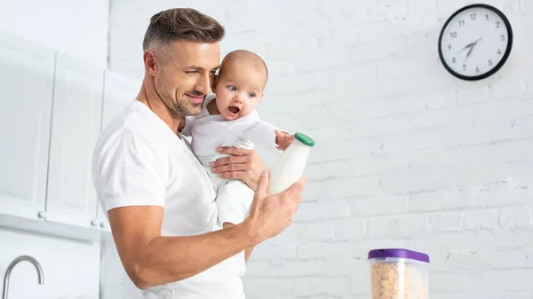 Vater hält Baby-Tochter und zeigt Flasche mit Milch — Stockfoto