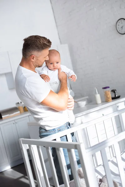 Padre sosteniendo hija bebé cerca de cuna en casa - foto de stock