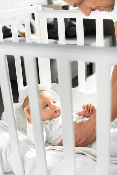 Cropped view of happy dad putting cheerful baby into baby crib — Stock Photo
