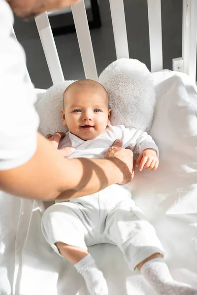 Cropped view of father putting cheerful baby into baby crib — Stock Photo