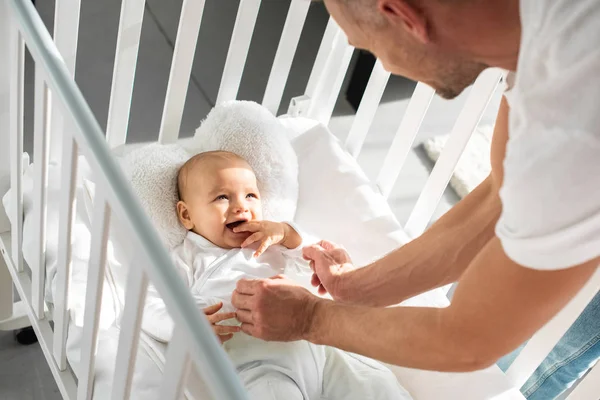 Cropped view of father putting infant daughter into baby crib — Stock Photo