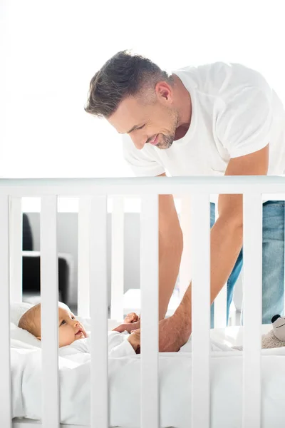 Веселий батько кладе немовляти доньку в дитяче ліжечко — стокове фото