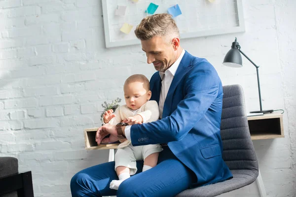 Handsome businessman showing watch to infant daughter in room — Stock Photo