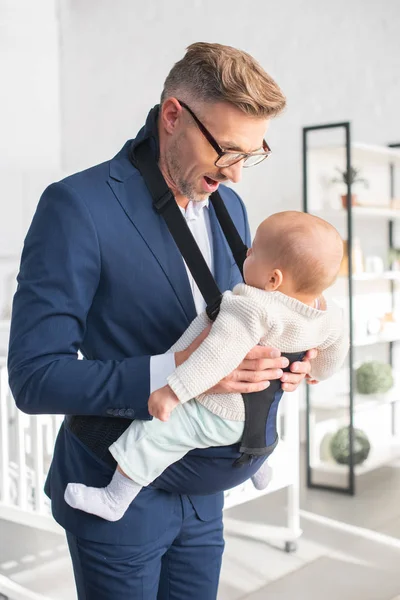 Happy businessman looking at infant daughter in baby carrier — Stock Photo