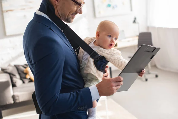 Geschäftsmann im Anzug hält Klemmbrett und kleine Tochter in Tragetasche — Stockfoto