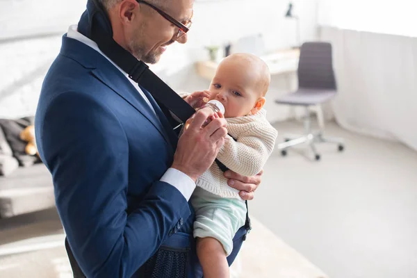 Businessman in suit feeding infant daughter from bottle — Stock Photo