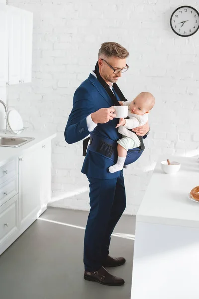 Homme d'affaires tenant fille en bas âge dans le porte-bébé et tasse avec boisson à la main — Photo de stock