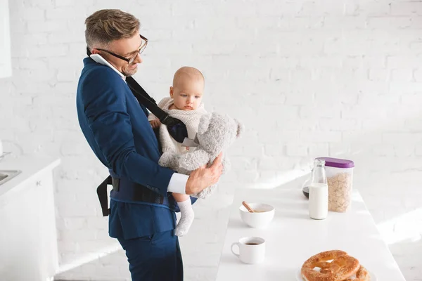 Бизнесмен разговаривает на смартфоне и держит в руках новорожденную дочь, глядя на плюшевого мишку — стоковое фото