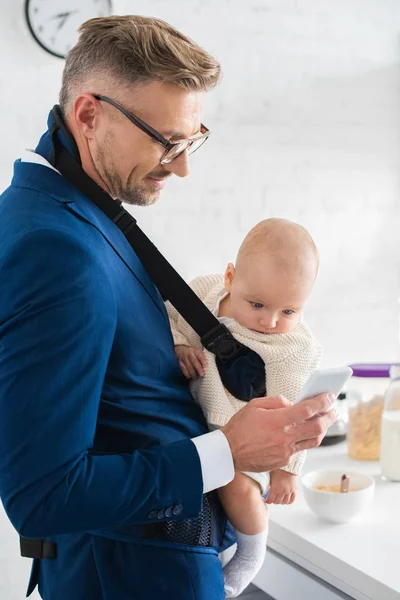 Веселий бізнесмен смартфон і дочка немовляти в дитячому перевізнику — стокове фото