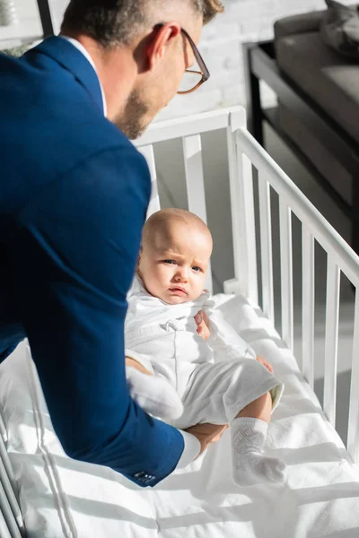 Father in suit putting infant daughter into baby crib — Stock Photo