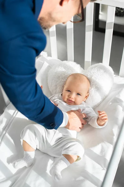 Обрезанный вид отца в костюме положить младенца дочь в кроватку — стоковое фото
