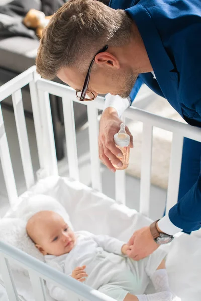 Selective focus of father in suit holding hand of infant daughter in baby crib — Stock Photo