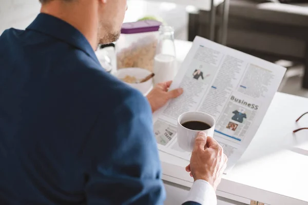 Обрезанный взгляд бизнесмена, читающего деловую газету и держащего кубок с кофе — стоковое фото