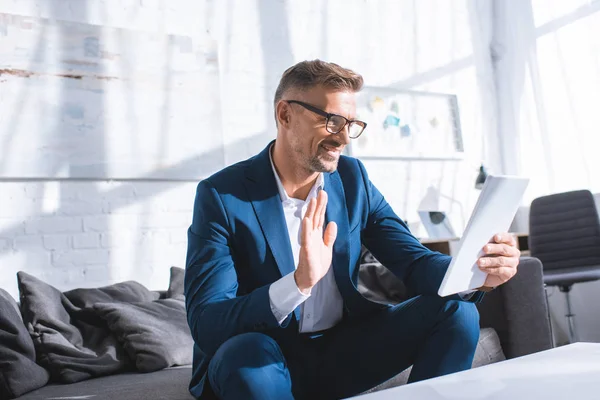 Feliz hombre de negocios saludando mientras tiene videollamada en la tableta digital - foto de stock