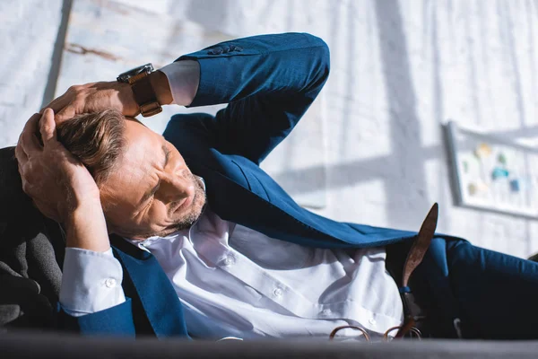 Hombre de negocios borracho teniendo dolor de cabeza mientras está acostado en el sofá - foto de stock