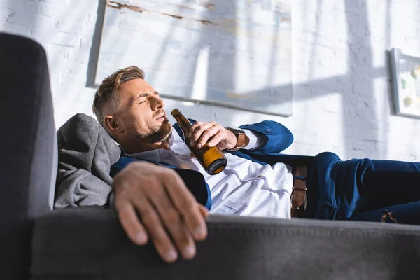 Betrunkener Geschäftsmann liegt mit geschlossenen Augen auf Sofa und trinkt Alkohol aus Flasche — Stockfoto