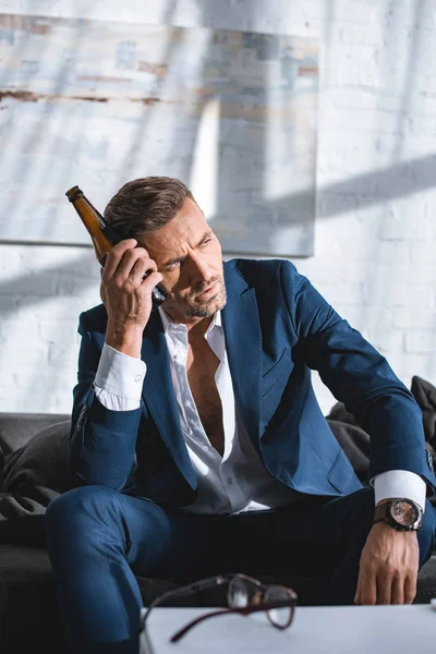 Drunk businessman holding bottle and sitting on sofa in living room — Stock Photo