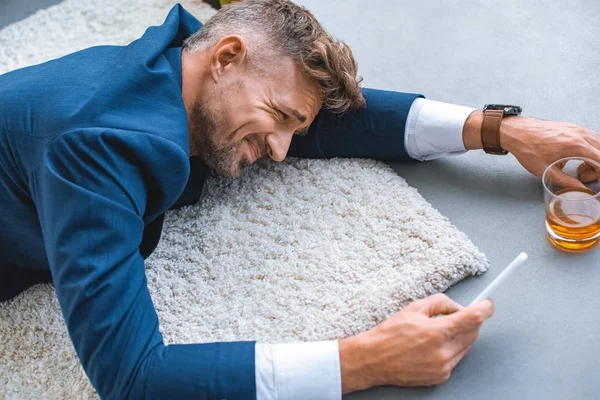 Drunk businessman lying on carpet with smartphone in hand — Stock Photo