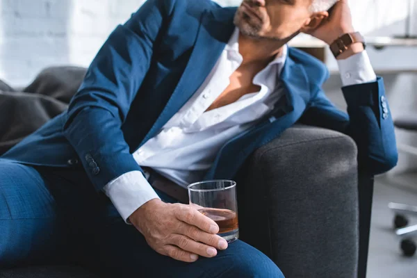 Vista recortada del hombre de negocios sosteniendo vidrio con bebida alcohólica - foto de stock