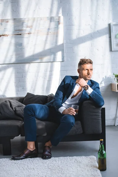 Hombre de negocios sentado en el sofá y sosteniendo vidrio con bebida alcohólica - foto de stock