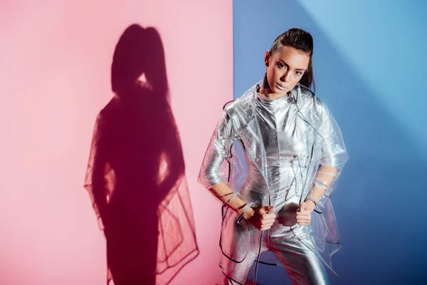 Fashionable girl posing in metallic bodysuit and raincoat on pink and blue background — Stock Photo