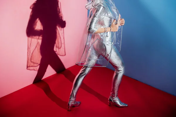 Vista cortada da menina elegante posando em bodysuit prata e capa de chuva no fundo rosa e azul — Fotografia de Stock