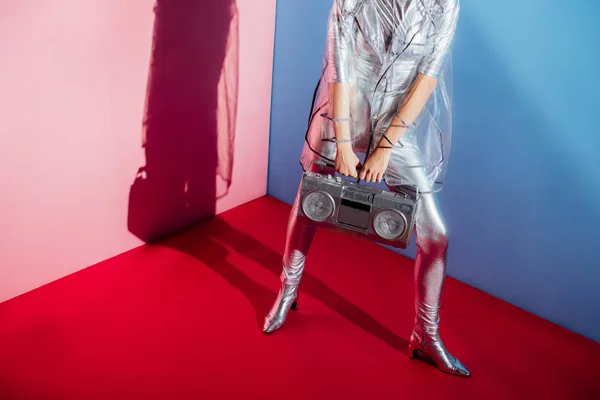 Cropped view of woman in metallic bodysuit and raincoat posing with boombox on pink and blue background — Stock Photo