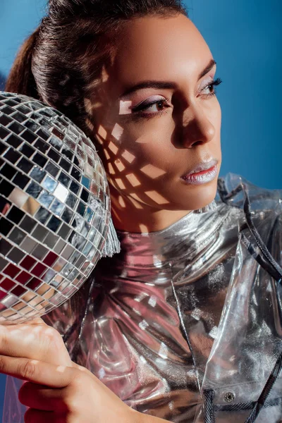 Привлекательная молодая женщина позирует с серебряным шаром диско на синем фоне — стоковое фото