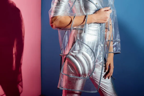Частичный вид модели в металлическом телесном костюме и дождевике с серебряными бананами для модной съемки на розовом и синем фоне — Stock Photo