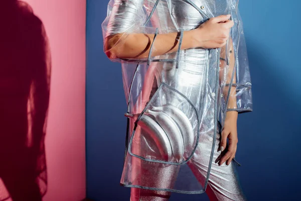 Partial view of model in metallic bodysuit and raincoat posing with silver bananas for fashion shoot on pink and blue background — Stock Photo