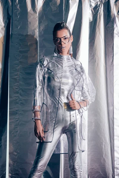 Attractive young model posing in silver bodysuit and raincoat on metallic background — Stock Photo