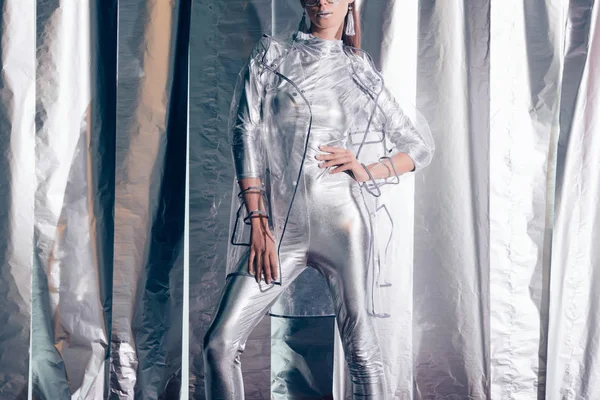 Abgeschnittene Ansicht einer jungen modischen Frau, die in silbernem Body und Regenmantel auf metallischem Hintergrund posiert — Stockfoto