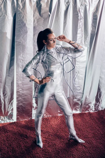 Приваблива молода жінка позує в срібному боді і плащі на металевому фоні — стокове фото