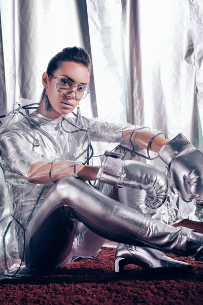 Modelo de moda posando en traje de cuerpo, impermeable y guantes de caja de plata sobre fondo metálico - foto de stock