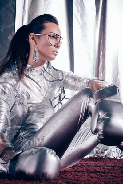 Young boxer posing in bodysuit, raincoat and silver box gloves on metallic background — Stock Photo