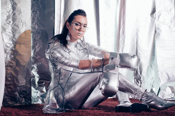 Brunette young woman posing in bodysuit, raincoat and silver box gloves on metallic background — Stock Photo