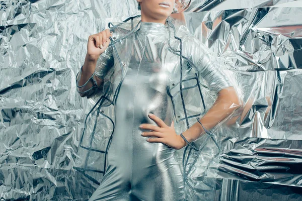 Vue recadrée de femme élégante posant en costume de corps argenté et imperméable sur fond métallique — Photo de stock